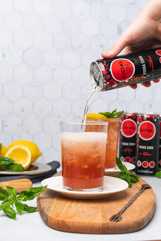 pouring social lite vodka soda into a glass with strawberry basil lemon sour mix