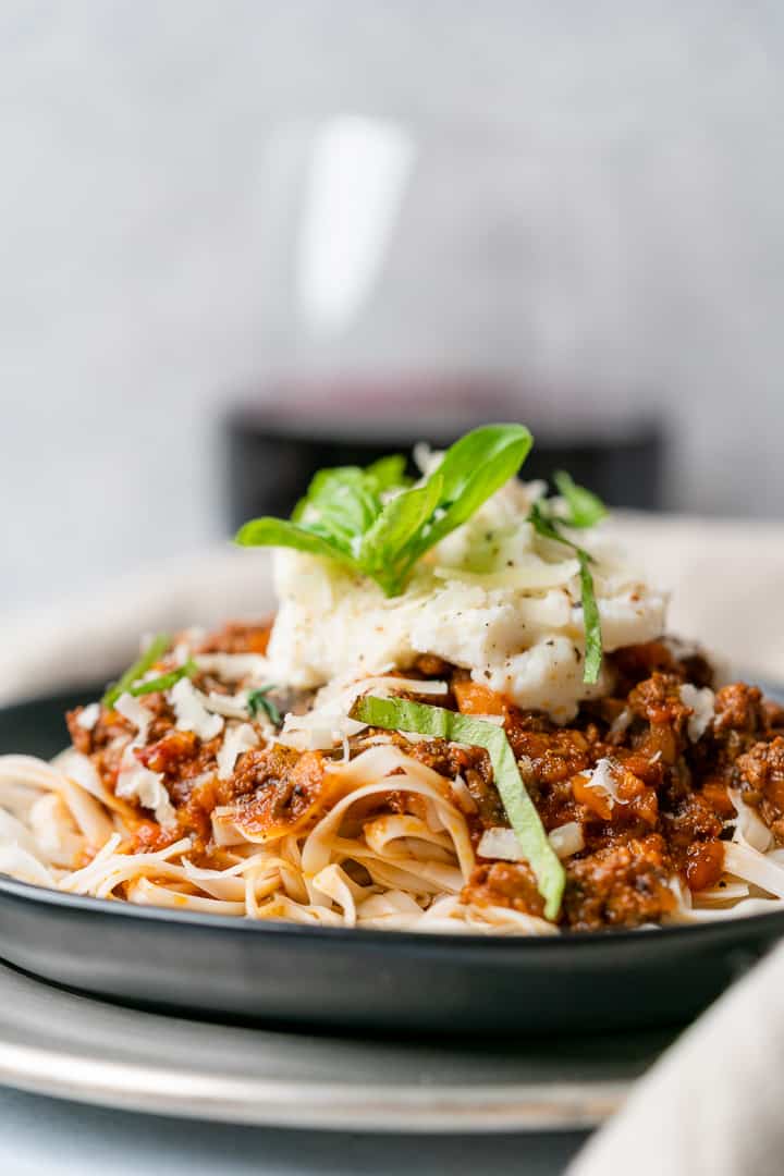 straight on shot of pasta with basil and ricotta cheese with wine in the background