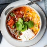 grey plate with grey bowl of turkey chili with cilantro sour cream and cheese