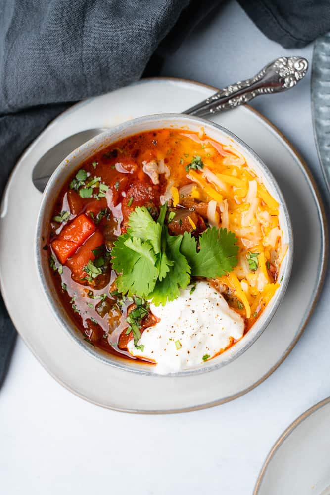 grey plate with grey bowl of turkey chili with cilantro sour cream and cheese