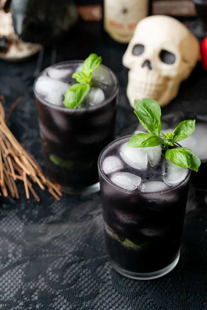two black spooky cocktails with a skull and broomstick