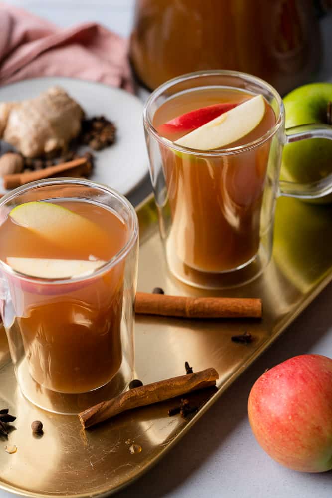 two glasses of spiced apple cider on a gold platter