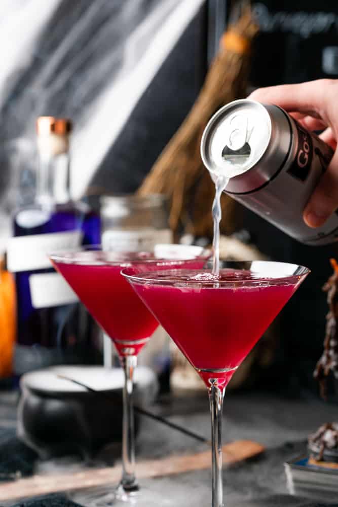 pouring diet ginger beer into a spooky purple cocktail