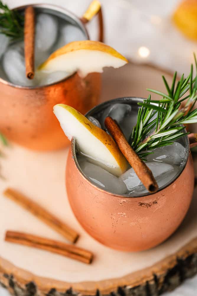 two copper mugs of spiced pear moscow mule with rosemary