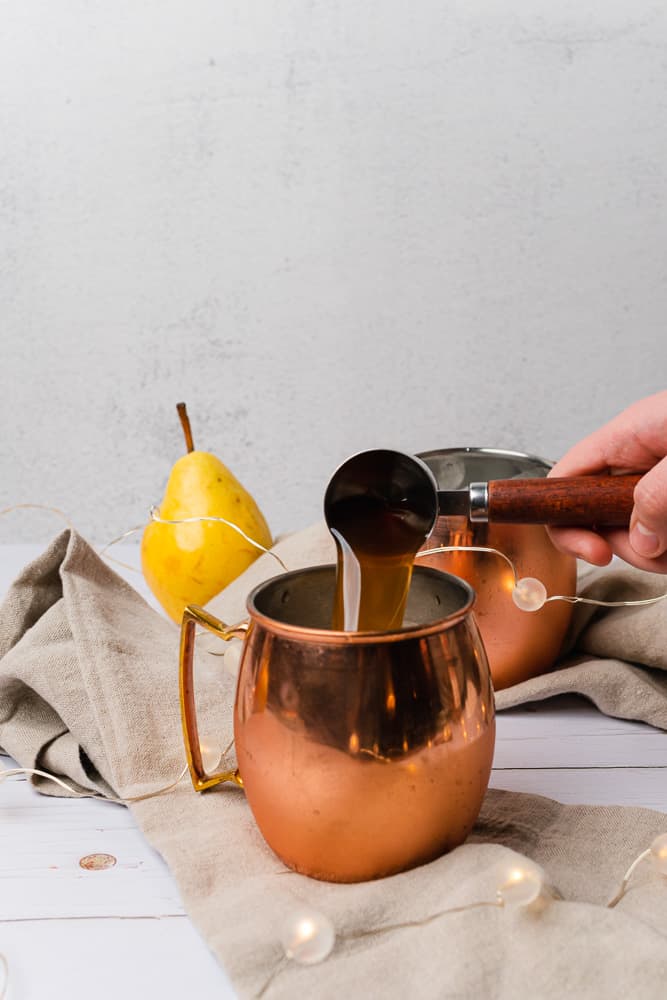 pouring spiced pear simple syrup into a moscow mule mug