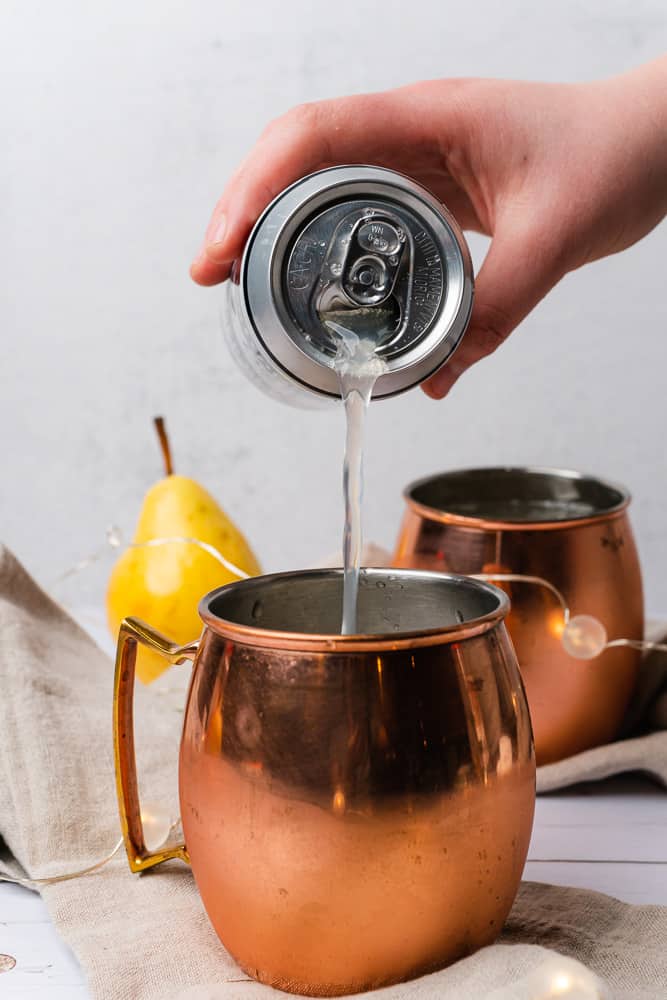 pouring ginger beer into a moscow mule mug