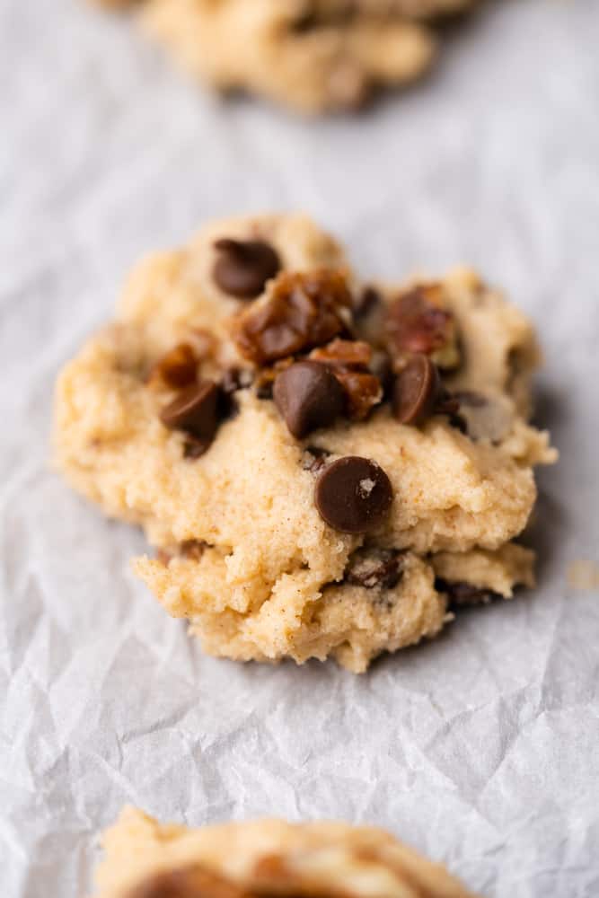 cookie dough on white parchment with candied pecans and chocolate chips