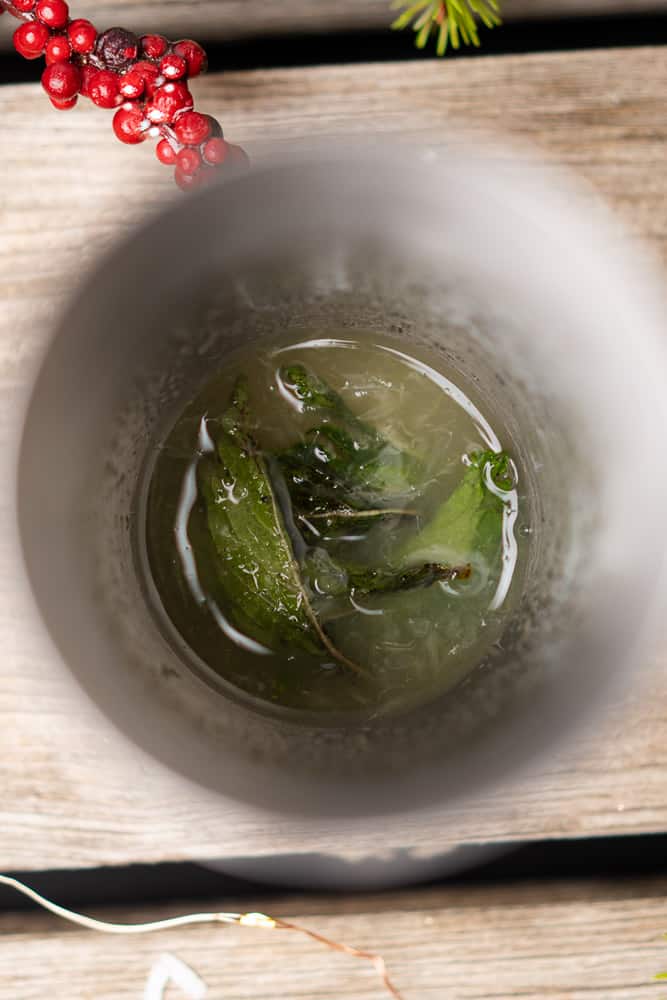 mint leaves lime juice and sweetener at the bottom of a cocktail shaker