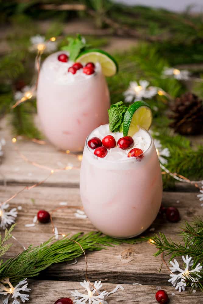 two glasses of light pink coconut mojito with garland cranberries and lights