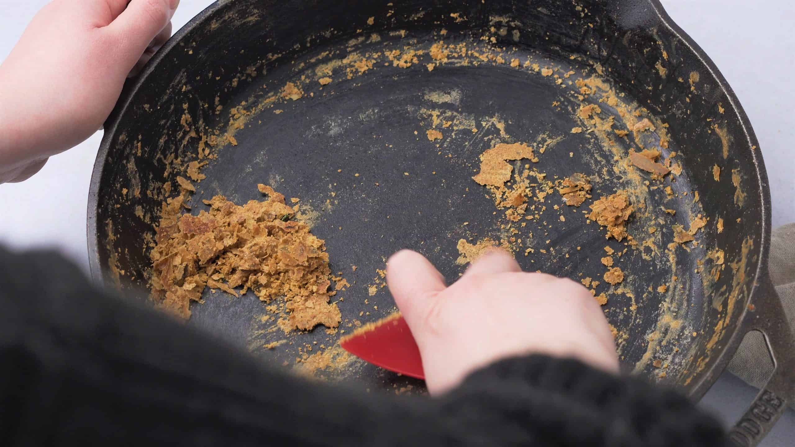 pieces of debris in a cast iron skillet with a scraper