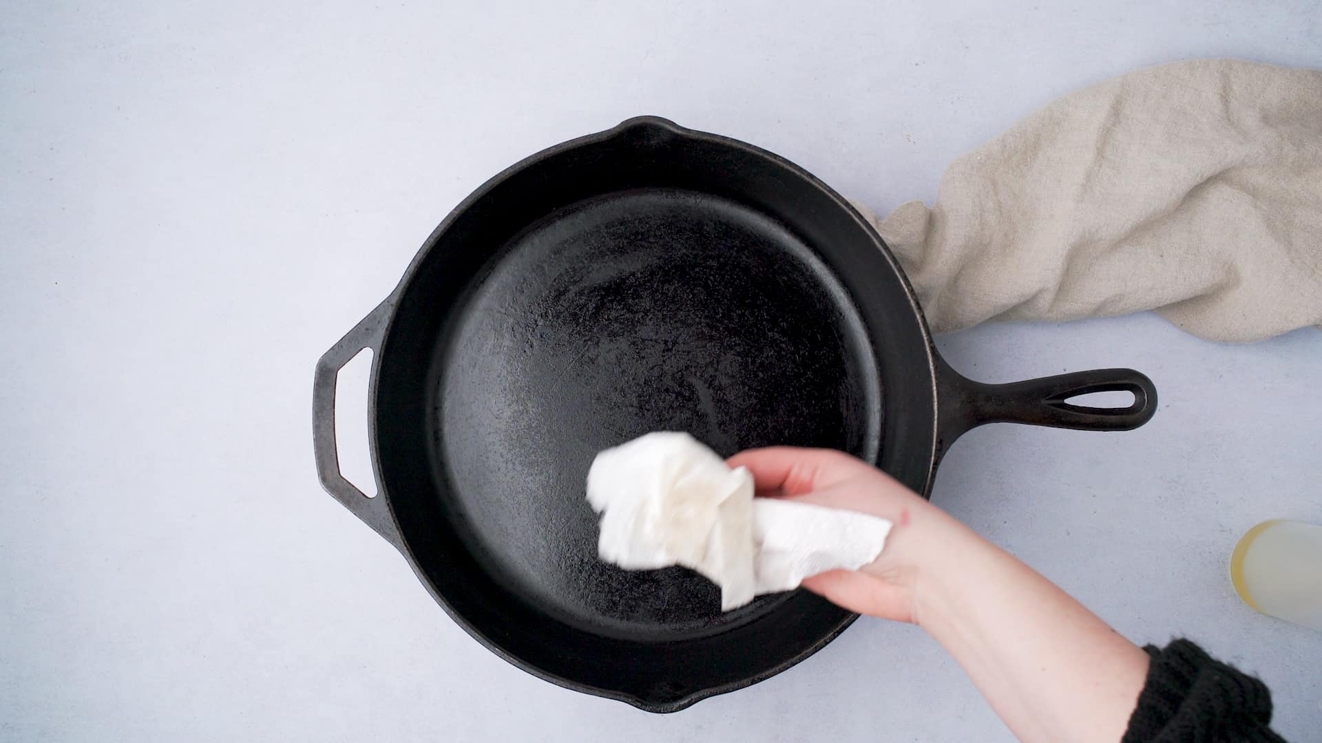 wiping a cast iron skillet with oil and a paper towel