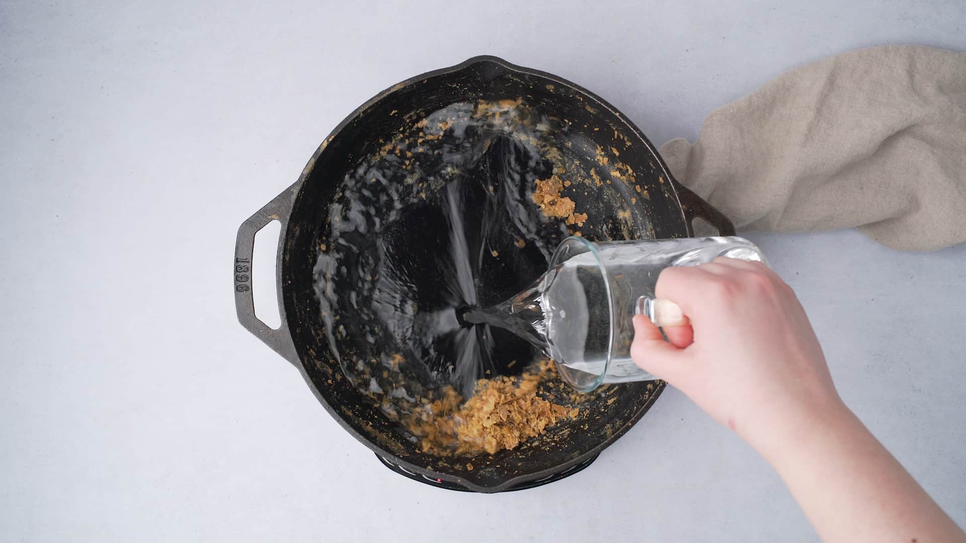 adding water to a cast iron skillet with food scraps in it 