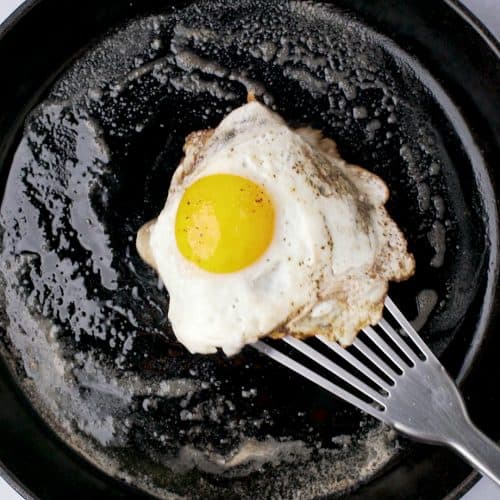 sunny side up egg with metal spatula in a cast iron skillet