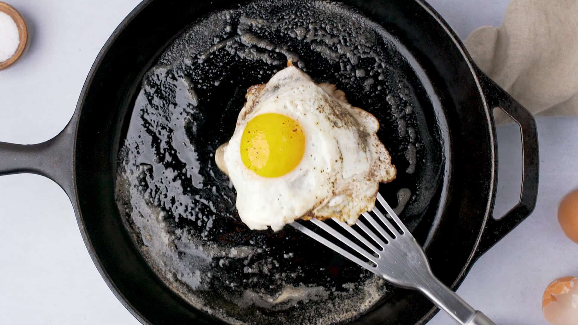 sunny side up egg with metal spatula in a cast iron skillet 