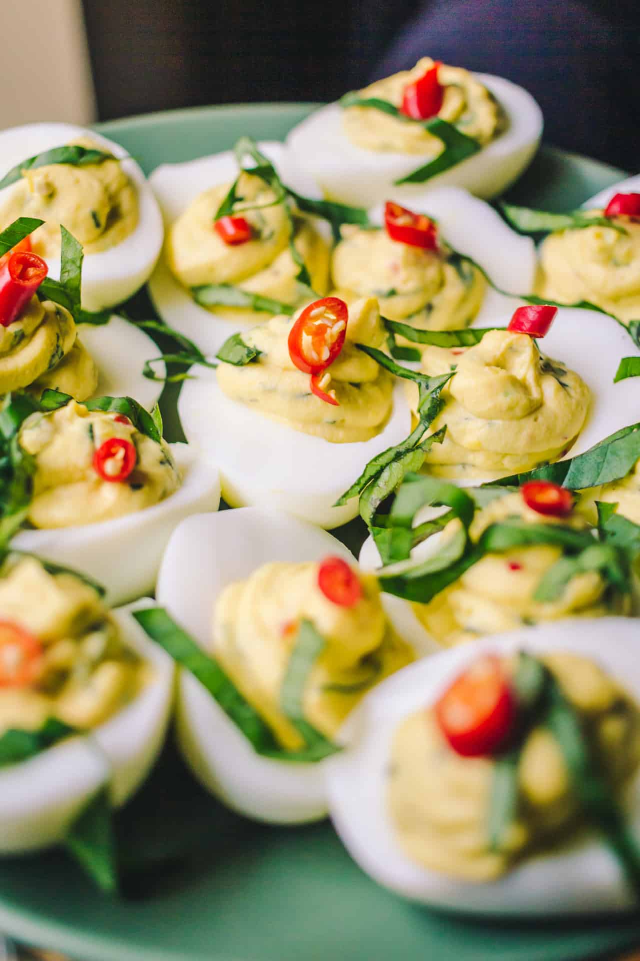 plate full of deviled eggs with red bird's eye chilis and thai basil