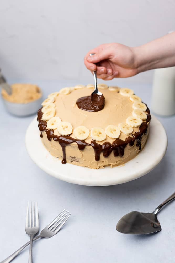 hand smoothing chocolate ganache to a banana cake 
