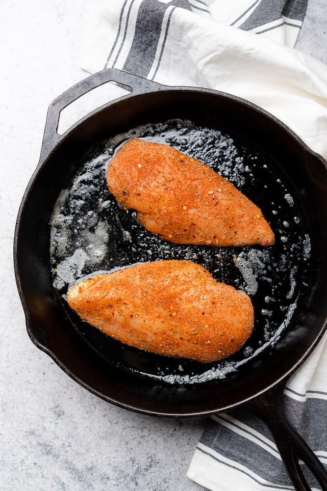 raw chicken breasts coated in cajun seasoning in a cast iron skillet 