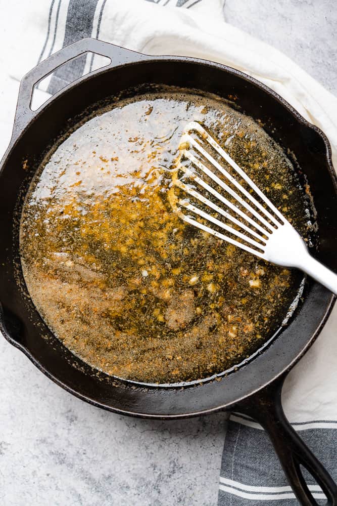 metal spatula stirring garlic and pan drippings with chicken broth