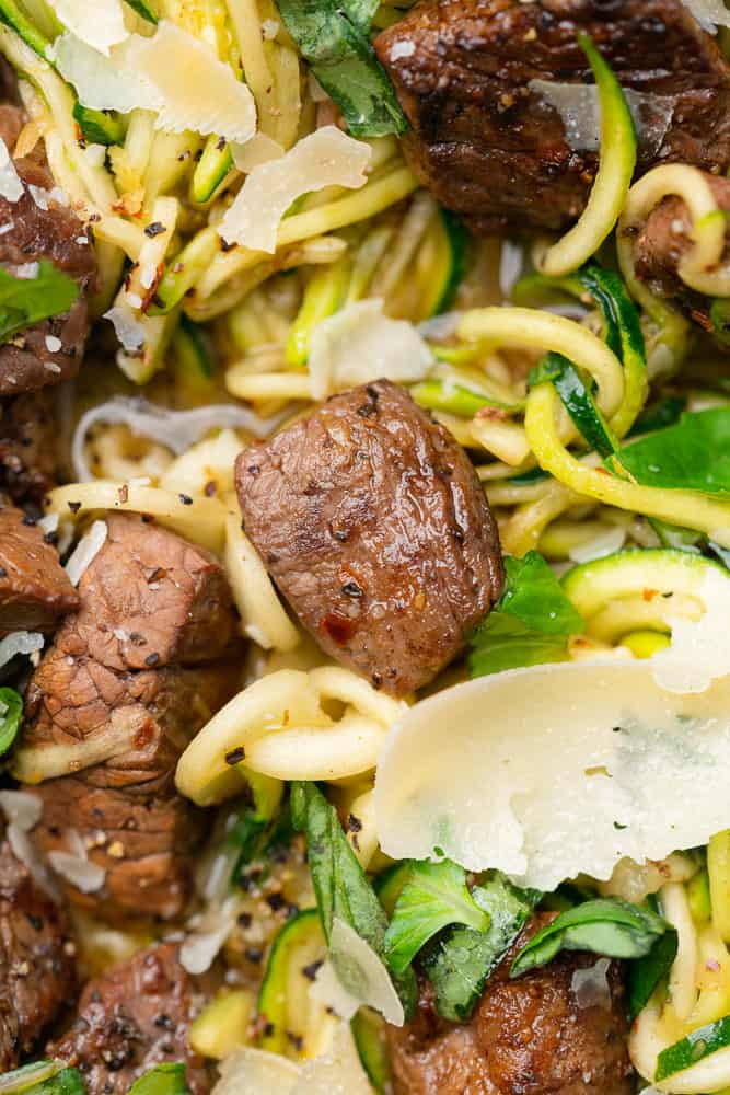 closeup shot of seasoned steak with zucchini noodles and parmesan cheese shreds