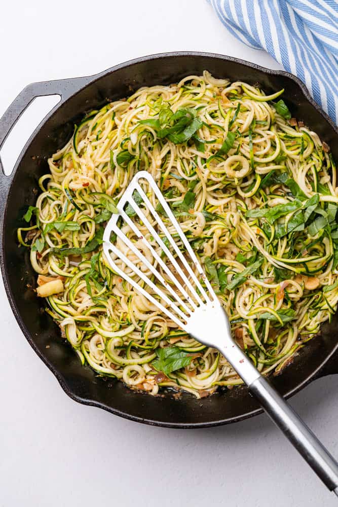 zucchini noodles with basil ribbons and a spatula in a cast iron skillet