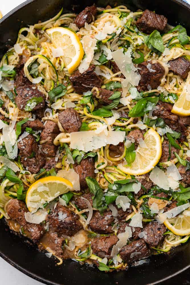 close up shot of garlic steak bites with lemon slices and zoodles