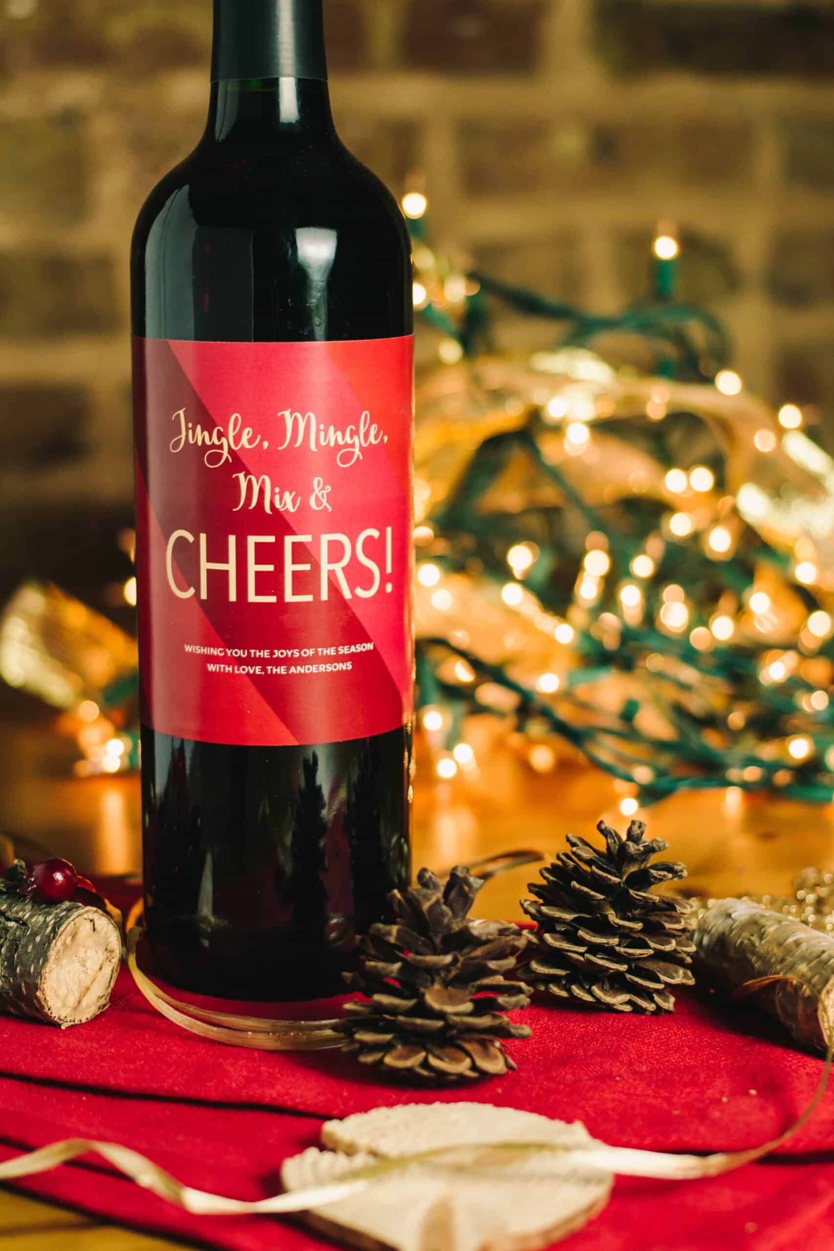 bottle of wine with text on it that says cheers with twinkling holiday lights and decorations in the background