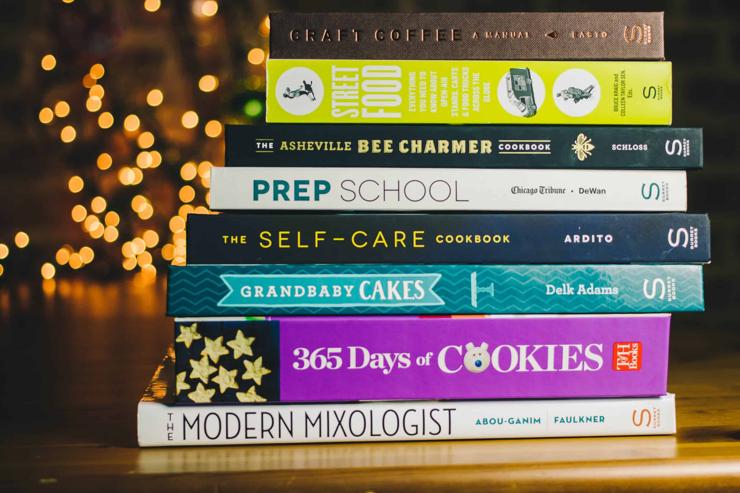 stack of cookbooks with twinkling lights in the background