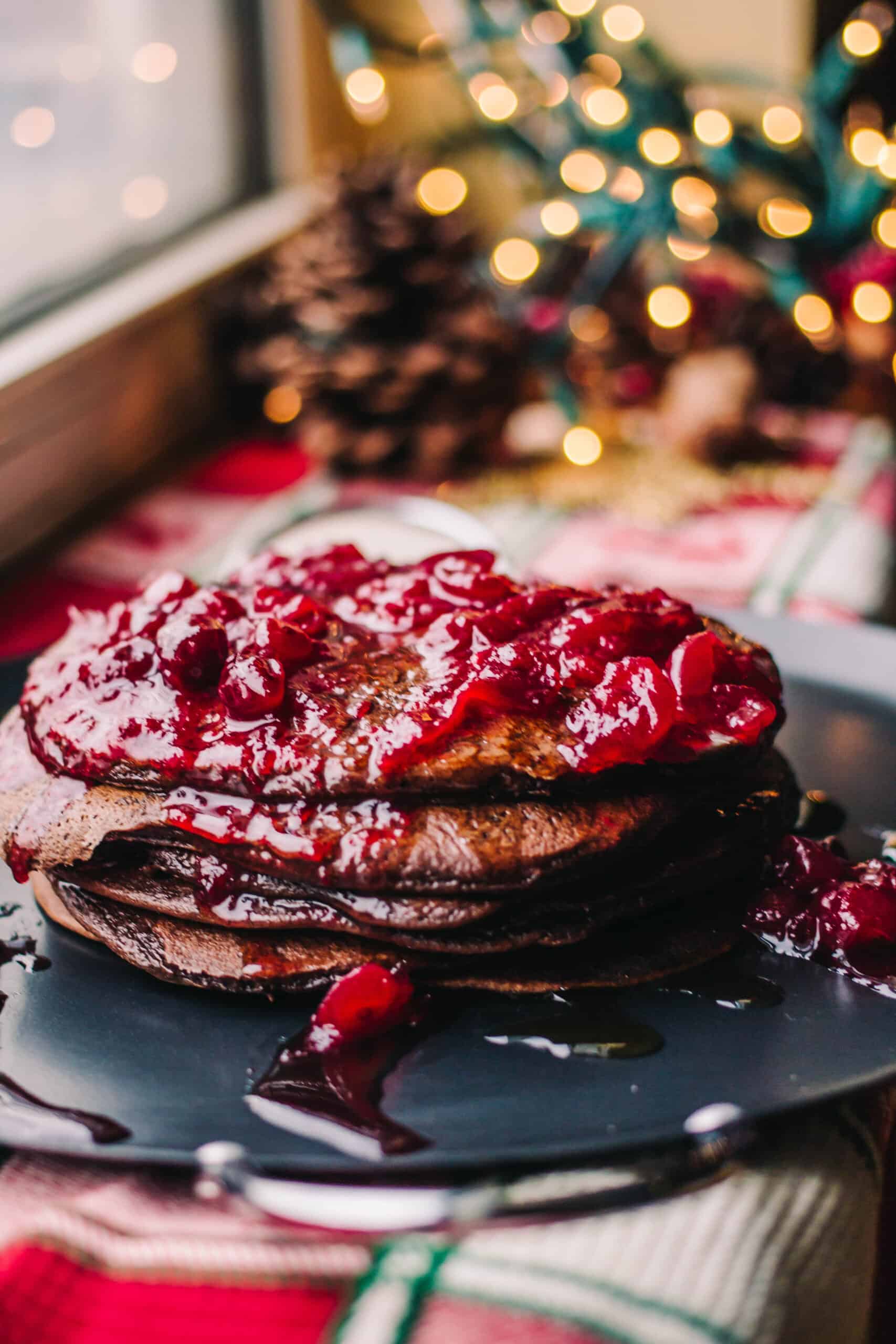 stack of chocolate pancakes with cherry topping and twinkling lights in the background