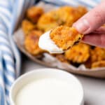 hand holding fried pickles dipped in ranch dressing with a light blue and white striped towel