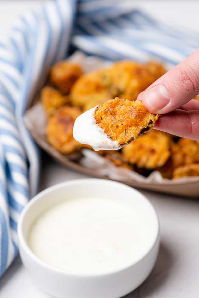 hand holding fried pickles dipped in ranch dressing with a light blue and white striped towel 