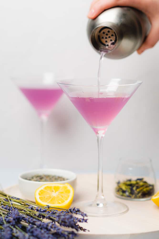 straining a light purple cocktail into a martini 