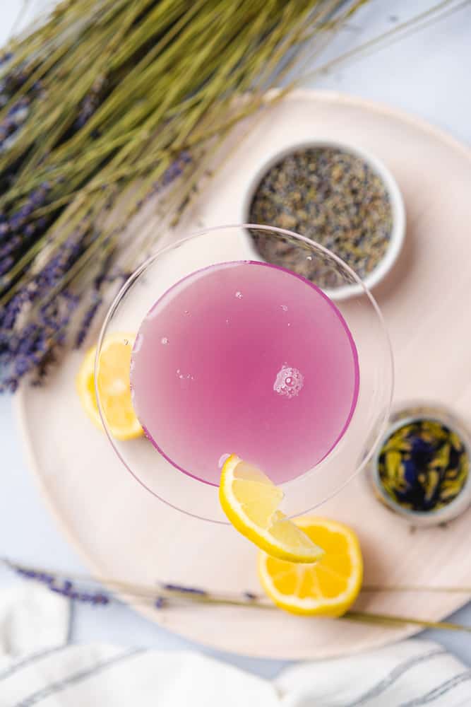 over head view of a lavender martini in a martini glass with lemons butterfly pea flower and dried lavender buds