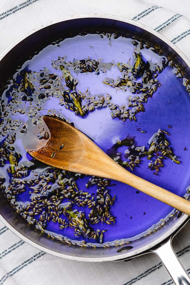 butterfly pea flowers and dried lavender in a bright indigo water in a sauce pan with a wooden spoon
