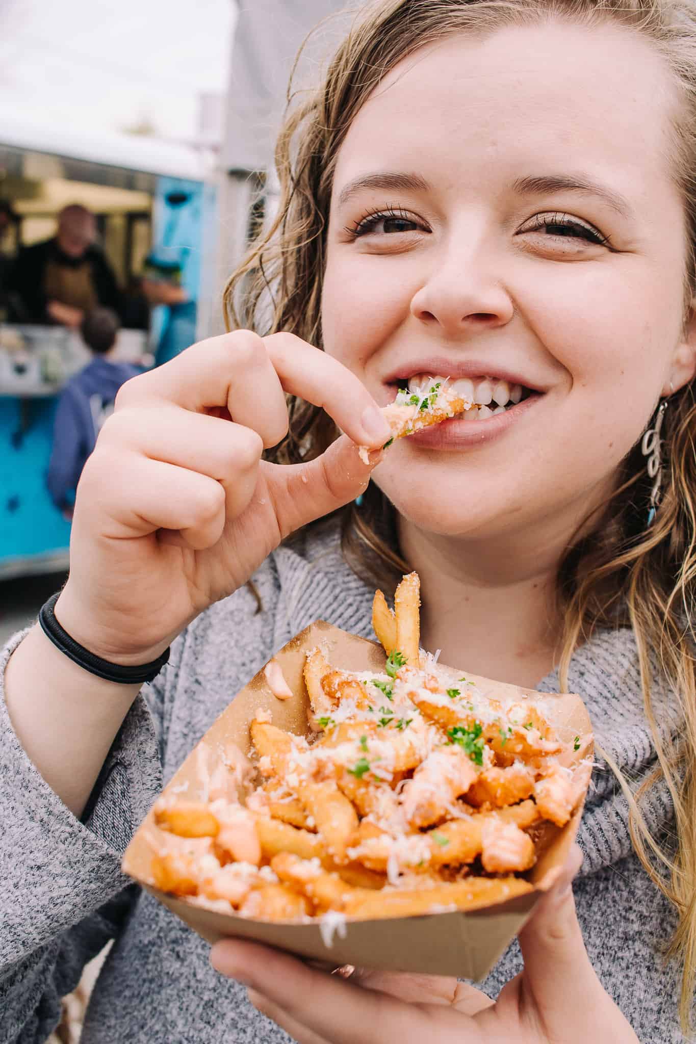 girl smiling while eating some loaded parmesan fries at the little fleet