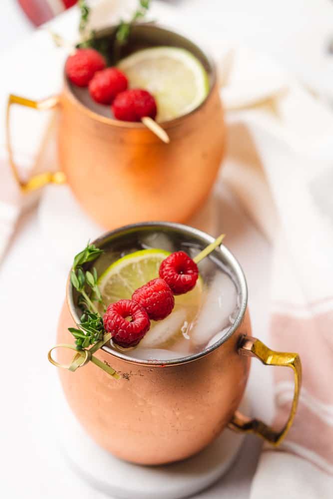 two copper mugs with raspberry moscow mules with fresh raspberries