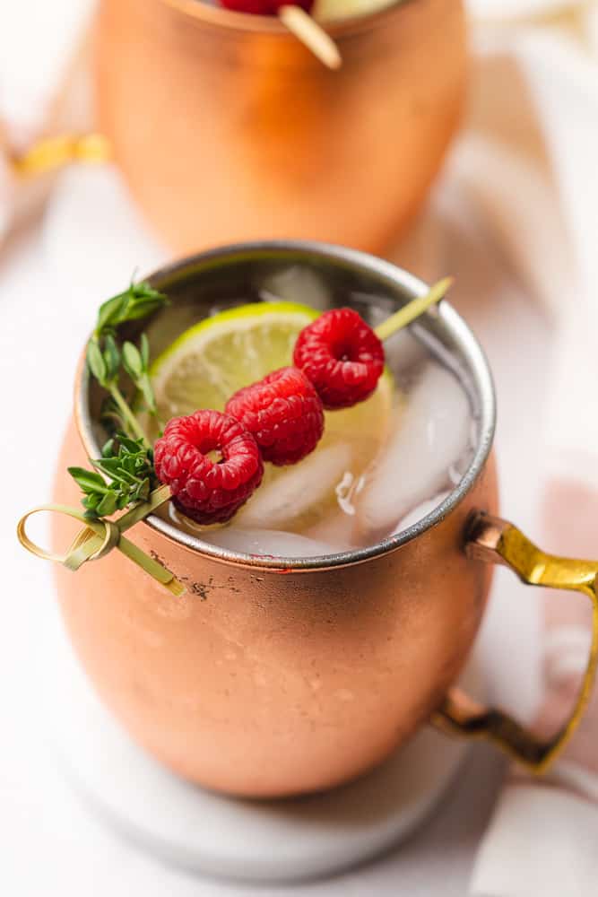 pretty sugar free raspberry moscow mule in a copper mug with fresh lime raspberries and thyme