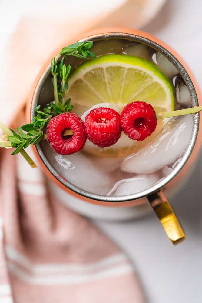 overhead view of a raspberry moscow mule with thyme springs and a pink and white napkin