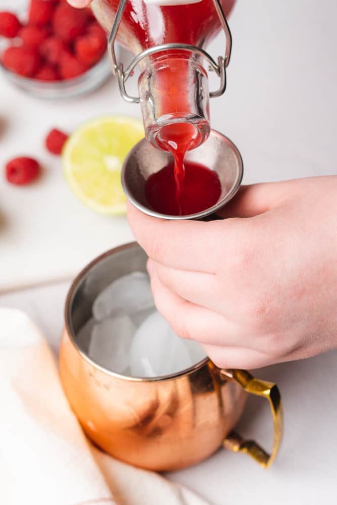pouring freshly made raspberry simple syrup into a copper moscow mule mug