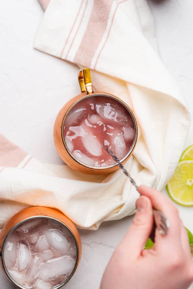 hand stirring moscow mule in a copper mug with raspberry simple syrup 