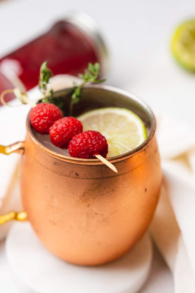 45 degree shot of raspberry moscow mule in a copper mug with fresh raspberries lime and thyme  