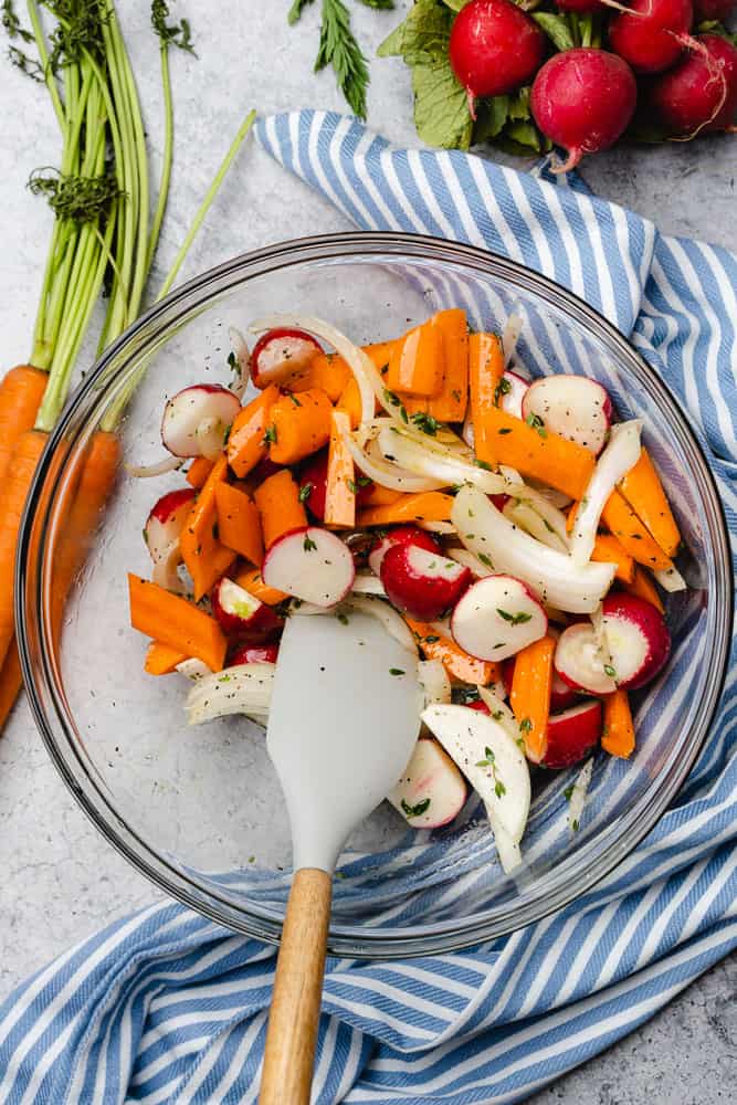 mixing vegetables together in a glass bowl with a rubber spatula