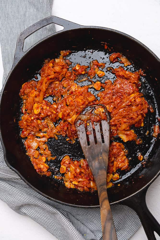 tomato paste in a cooked mixture of shallots and garlic in a cast iron skillet
