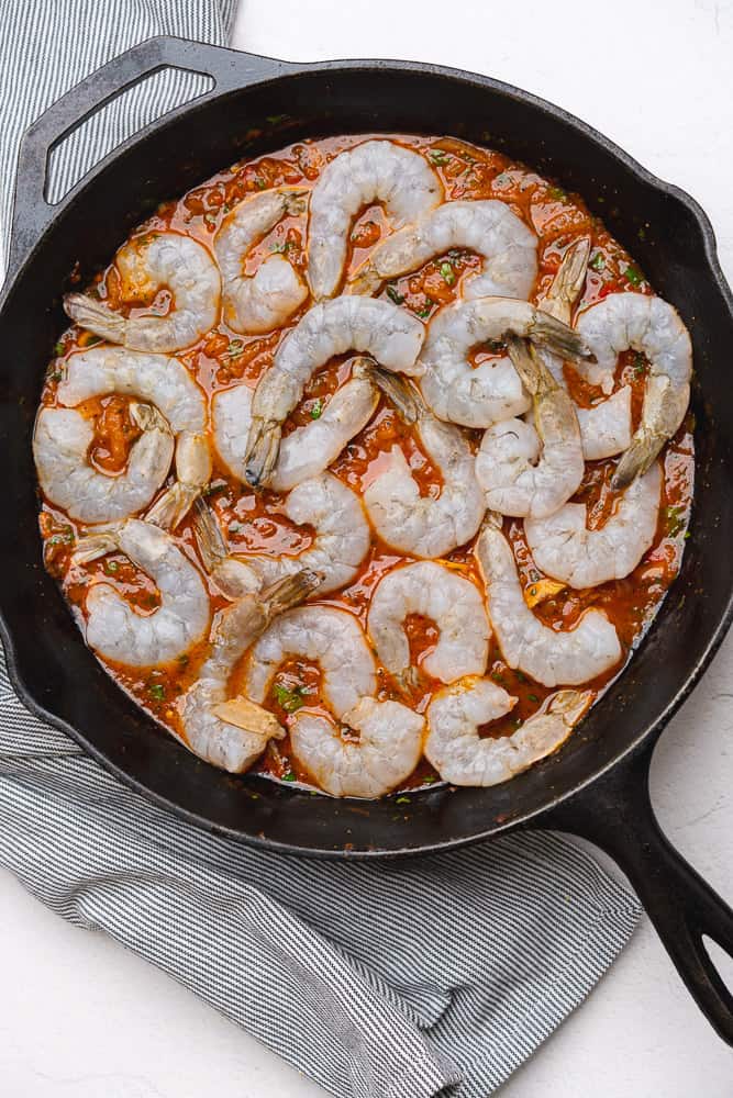 raw shrimp cooking for shrimp and caramelized shallot pasta in a cast iron skillet