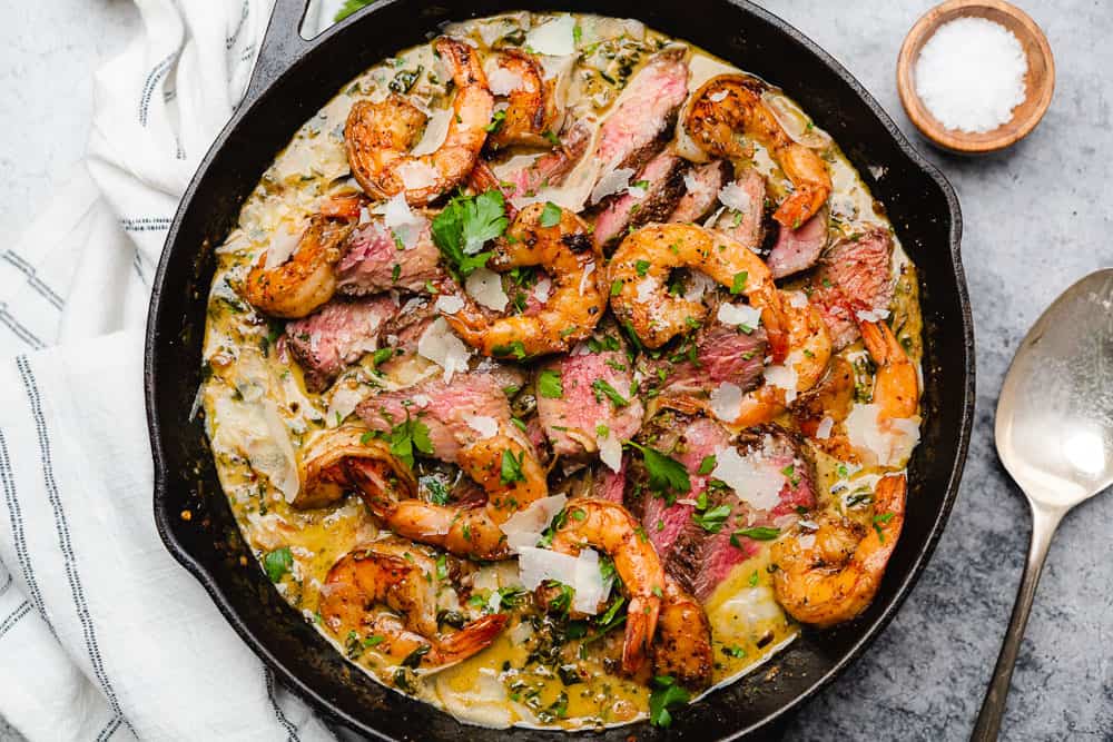 skillet filled to the brim with a creamy sauce medium rare steak and shrimp