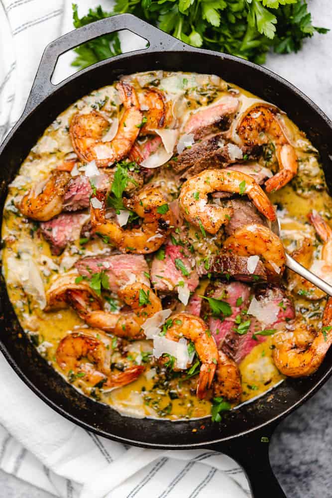 cast iron skillet with steak shrimp and creamy garlic parmesan sauce with spinach