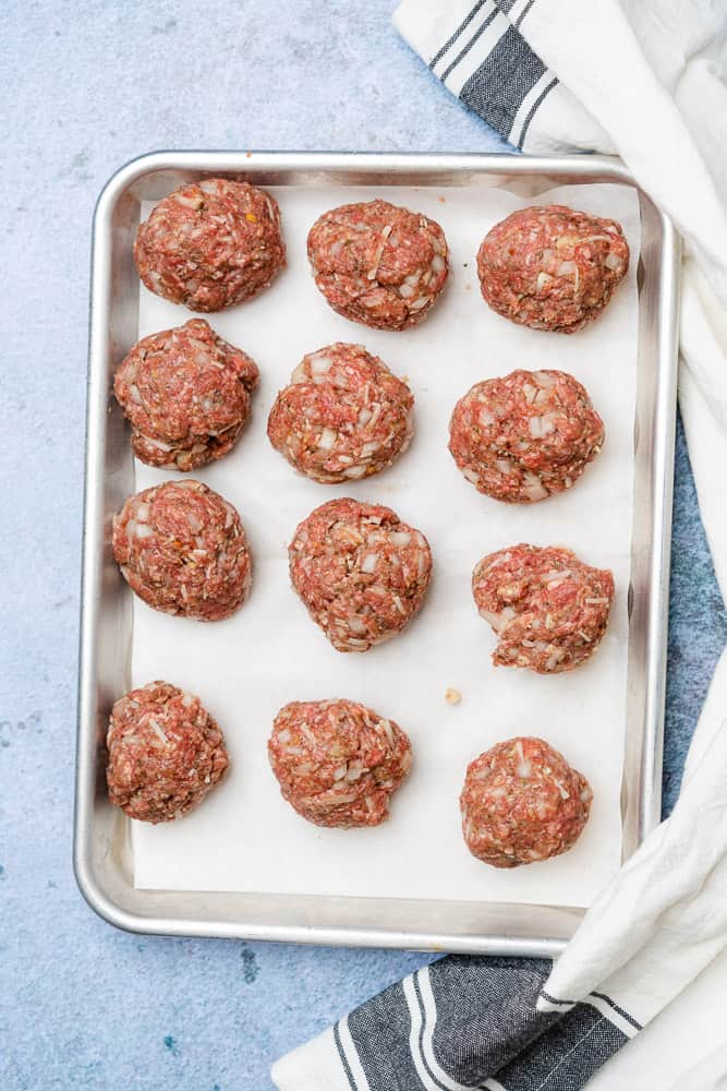 raw meatballs rolled into meatball shape on a parchment lined baking sheet