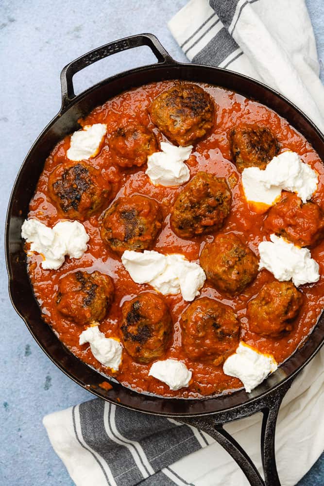 meatballs in a cast iron skillet with dollops of ricotta cheese