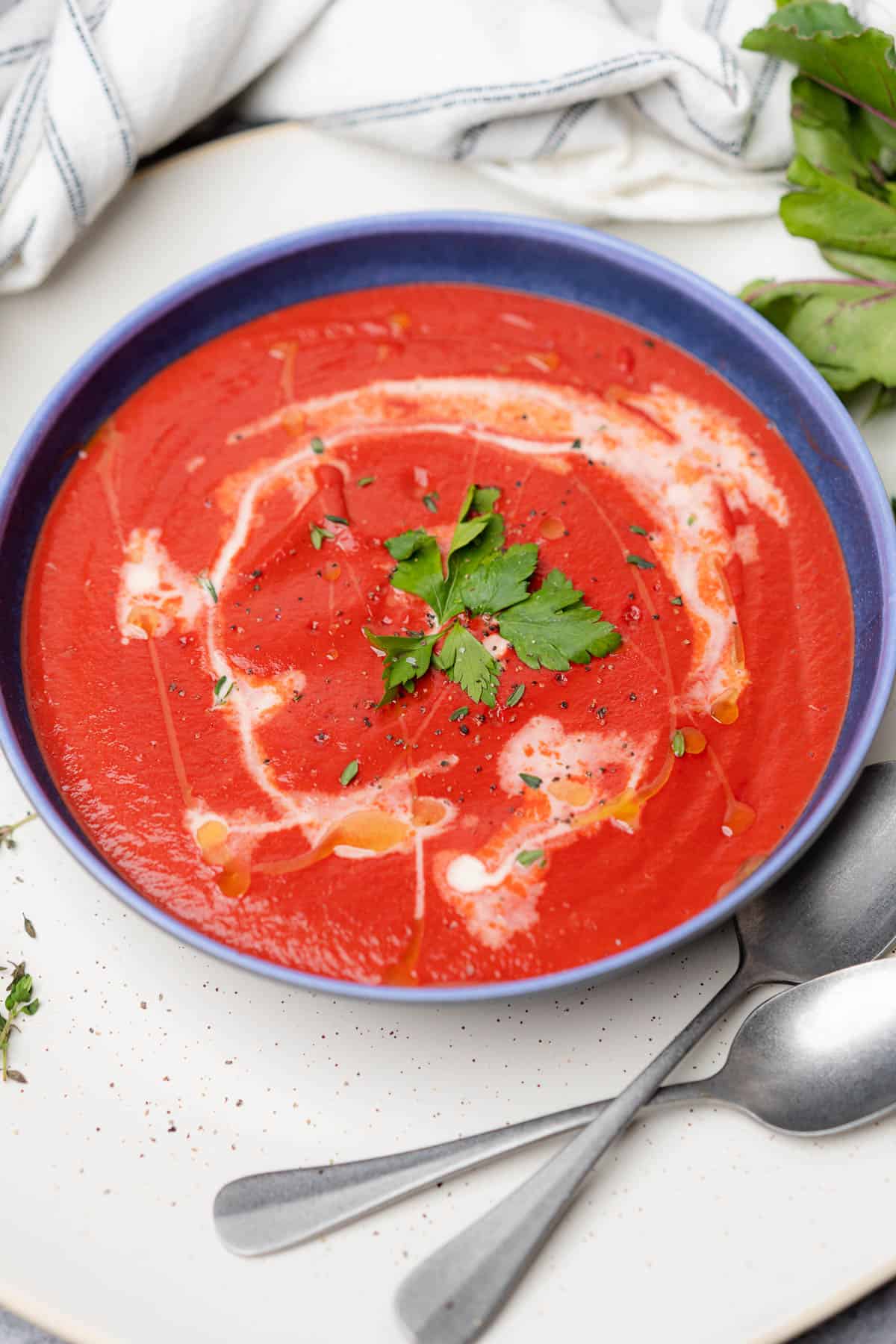 bowl of bright red beetroot carrot soup with heavy cream and parsley 