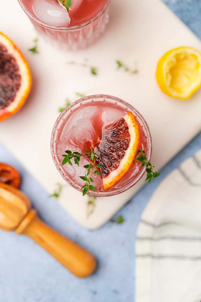 overhead view of blood orange gin cocktail with thyme sprigs and a citrus reamer