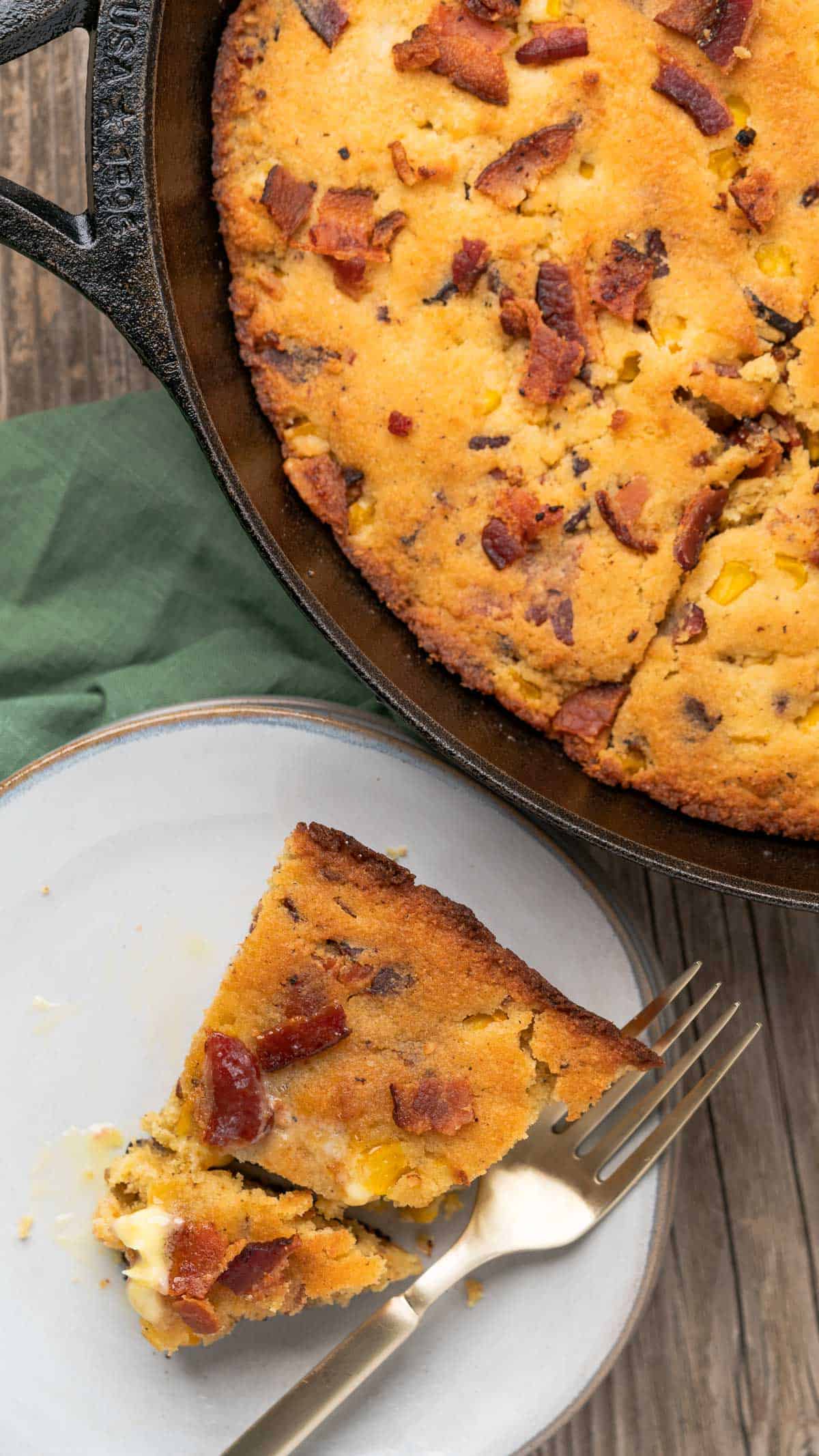brown butter cornbread with bacon with a bite cut out of it and a skillet closeby
